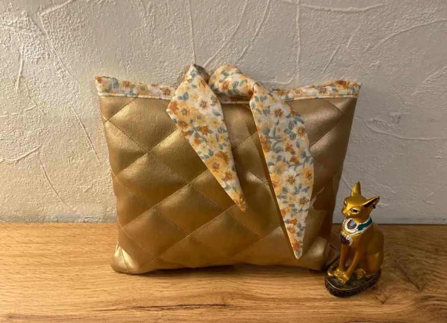 Pochette liseuse ou livre de poche dorée matelassée avec tissu fleuri, posée sur bois