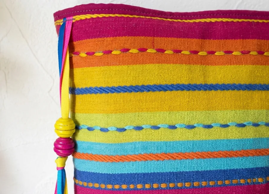 Gros plan des pompons colorés et rayures vives de la pochette tissu cousue main Créa'Flo