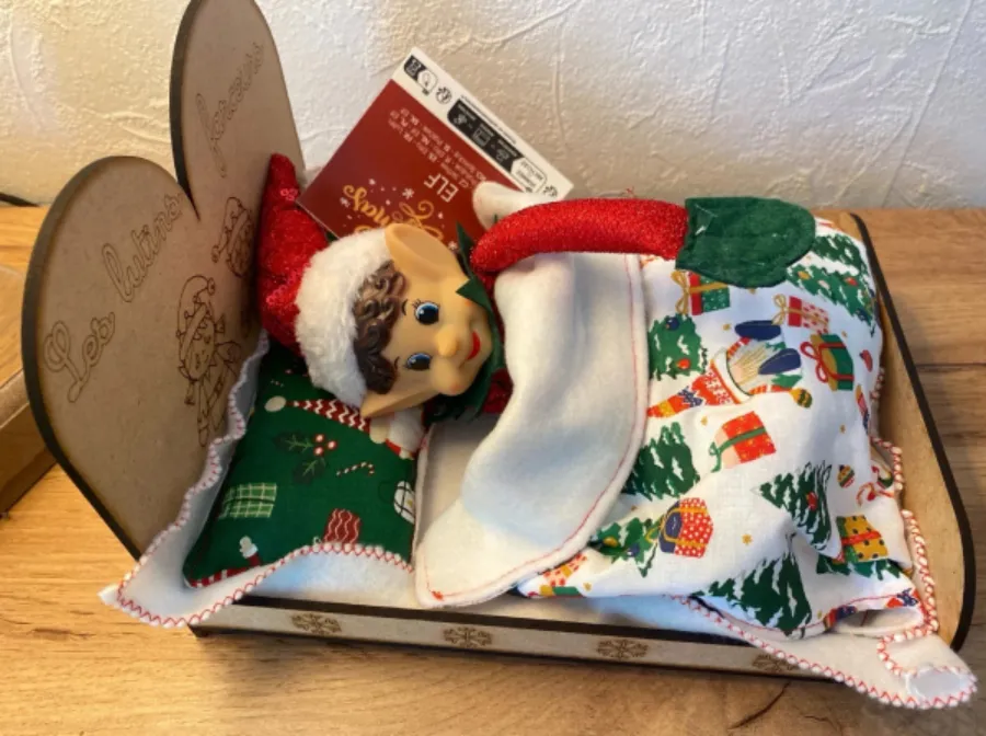 Lutin farceur de Noël installé dans son lit en bois MDF gravé, avec linge cousu main motifs Noël