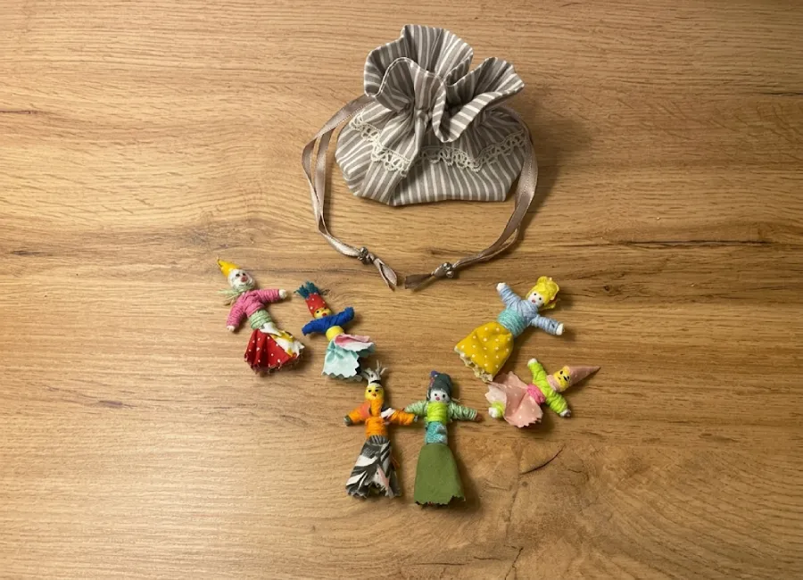 Pochette en tissu rayé beige et ses poupées tracas artisanales colorés disposés sur bois, Créa'Flo